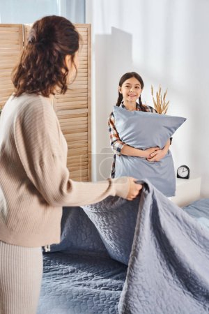 A girl holds a pillow, showcasing a tender moment between a mother and daughter at home.