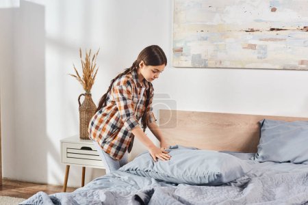 girl in plaid shirt and jeans arranging pillows on bed in cozy home setting.