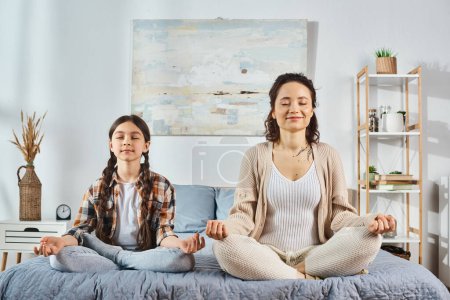 Foto de Un vínculo madre e hija mientras practican yoga juntos en una acogedora cama en casa, fomentando la conexión y el bienestar. - Imagen libre de derechos