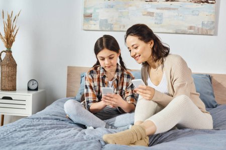 Photo for Mother and daughter, sit on a bed, engrossed in a cell phone, sharing a moment of connection. - Royalty Free Image