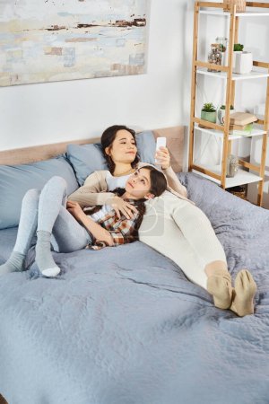 Téléchargez les photos : Une mère et sa fille, se blottissant et se relaxant sur un lit confortable dans une étreinte chaleureuse et aimante. - en image libre de droit