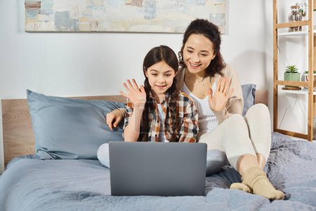 Mutter und Tochter sitzen auf einem Bett, vertieft in die gemeinsame Benutzung eines Laptops.