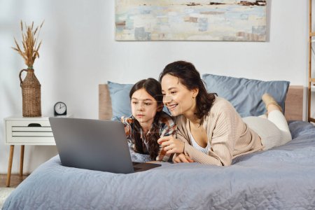 Téléchargez les photos : Mère et fille se détendre sur un lit, absorbé dans un écran d'ordinateur portable. - en image libre de droit