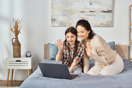 Téléchargez les photos : Mère et fille, partageant un ordinateur portable assis sur un lit confortable dans un cadre familial. - en image libre de droit