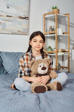 Ein Mädchen sitzt gemütlich auf einem Bett, hält einen Teddybär dicht an der Brust und genießt einen ruhigen und friedlichen Moment