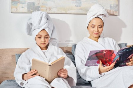 A brunette mother and her daughter in white bath robes, sitting peacefully on top of a bed.