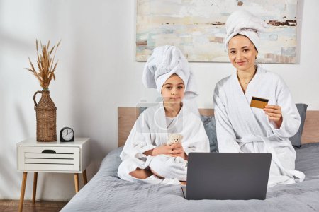 Foto de Madre e hija vestidas con batas blancas, sentadas en una cama, compartiendo un momento especial juntas. - Imagen libre de derechos