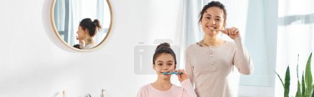 Eine brünette Frau und ihre halbwüchsige Tochter gehen ihrer Morgenroutine nach und putzen sich in einem modernen Badezimmer die Zähne.