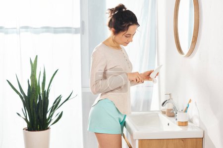 A brunette woman stand in front of a bathroom sink, engaging in beauty and hygiene routine.