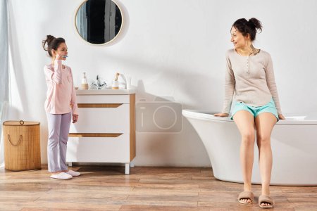 Téléchargez les photos : Une femme brune se tient à côté de sa fille préadolescente dans une salle de bain moderne, s'engageant dans des routines de beauté et d'hygiène. - en image libre de droit