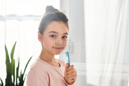 A brunette preteen girl holding a toothbrush in a modern bathroom, emphasizing the importance of hygiene routine.