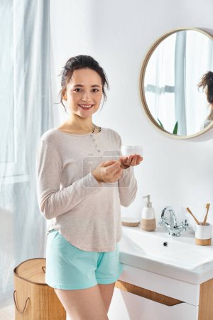 Photo for A brunette woman stand in front of a modern bathroom sink, engaging in their beauty and hygiene routine. - Royalty Free Image