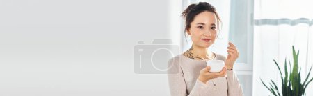 Téléchargez les photos : Une femme brune tient un pot de crème, regardant directement la caméra avec une expression sereine sur son visage. - en image libre de droit