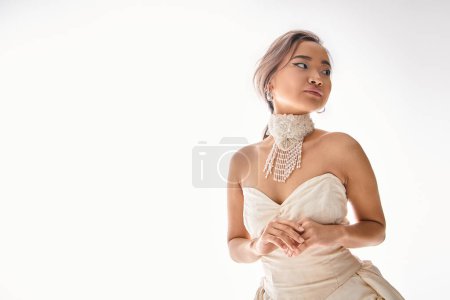 Photo for Elegant asian young woman in white dress restrained posing and looking to side on white background - Royalty Free Image