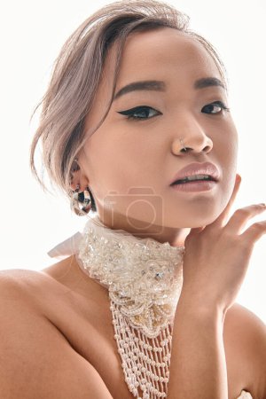 Téléchargez les photos : Gros plan de grâce asiatique mariée avec luxe collier cadrage avec les mains pour faire face sur fond blanc - en image libre de droit