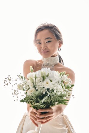 Foto de Atractivo joven asiático mujer con gracia maquillaje mantenga fuera ramo de flores blancas sobre fondo claro - Imagen libre de derechos