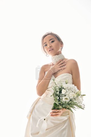 attractive asian woman touch to white necklace and hold out bouquet of flowers on light background