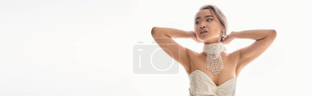 Photo for Horizontal shot of asian woman in stylish necklace looking to side and putting hands behind head - Royalty Free Image
