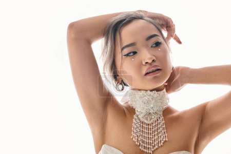 Téléchargez les photos : Séduisante asiatique jeune femme avec élégant maquillage regardant à côté et mettre les mains derrière la tête - en image libre de droit