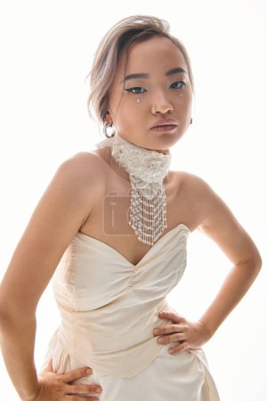 confident asian young bride in elegant  necklace and dress posing on white background