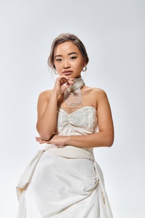 anmutige asiatische junge Frau in elegantem Kleid mit nachdenklichem Gesichtsausdruck auf hellem Hintergrund