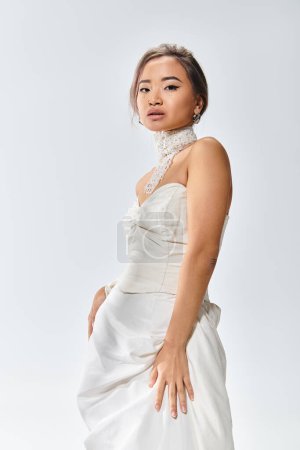 Téléchargez les photos : Charmante asiatique jeune femme en blanc élégant robe confiant posant sur fond clair - en image libre de droit