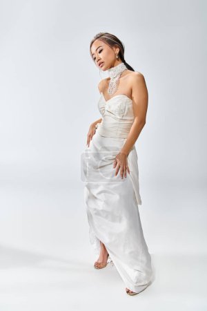 pretty asian woman in white elegant dress posing and looking to down on light background