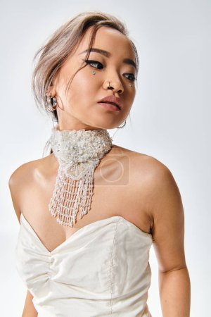 Téléchargez les photos : Portrait de élégant asiatique jeune femme en blanc grâce collier regardant en arrière sur fond clair - en image libre de droit