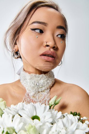 Téléchargez les photos : Charmante femme asiatique dans sa vingtaine avec des fleurs blanches regardant vers le côté sur fond clair - en image libre de droit