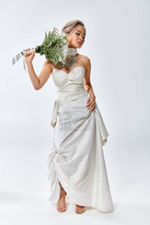 hübsche junge Braut im weißen eleganten Outfit posiert mit Blumenstrauß und schaut nach unten