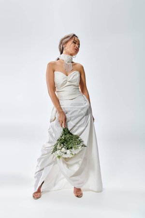 attraktive junge Braut im weißen eleganten Outfit dreht den Kopf und posiert mit Blumenstrauß