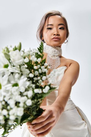 Foto de Encantadora mujer asiática en su 20s sostienen a blanco flores ramo en fondo claro - Imagen libre de derechos