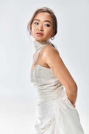 atractiva mujer asiática en collar blanco de pie de lado inclinado hacia adelante y mirando hacia atrás