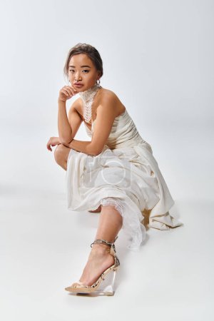 atractivo asiático joven mujer en blanco elegante vestido agachado abajo y estirado pierna fuera en frente