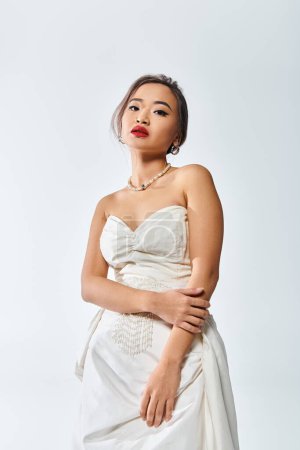 hübsche asiatische junge Frau mit roten Lippen und Perlenkette posiert auf weißem Hintergrund