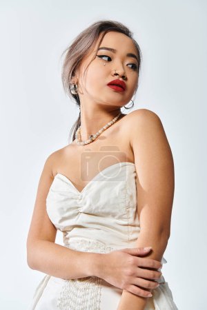 Photo for Alluring asian woman in her 20s with red lips and pearl necklace look to side on white background - Royalty Free Image