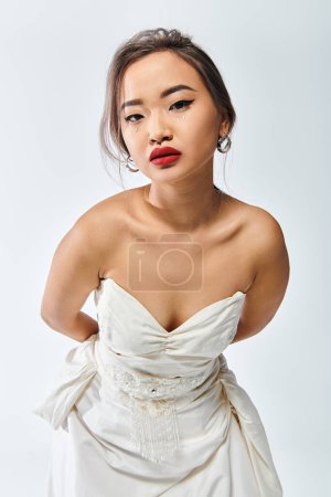 schöne asiatische Frau in ihren Zwanzigern mit rotem Lippenstift lehnt sich nach vorne auf weißem Hintergrund