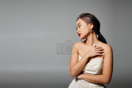 Photo for Alluring woman with red lips covering to neckline and looking to side against grey background - Royalty Free Image