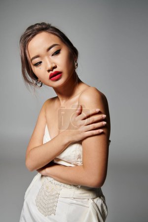 portrait of asian woman in her 20s holding to shoulder and looking to back on grey background