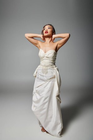 elegant asian young girl in bridal outfit with red lips putting hand behind head and looking to up
