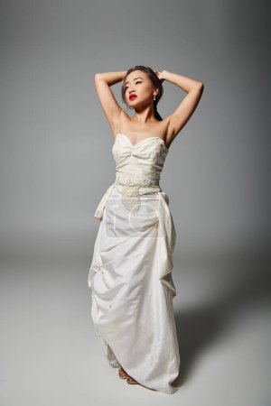 atractiva mujer joven asiática en vestido blanco con labios rojos poniendo la mano detrás de la cabeza y mirando hacia arriba