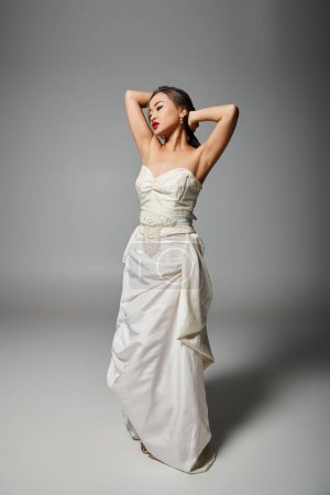 pretty asian woman in white dress with red lips putting hand behind head and looking to down