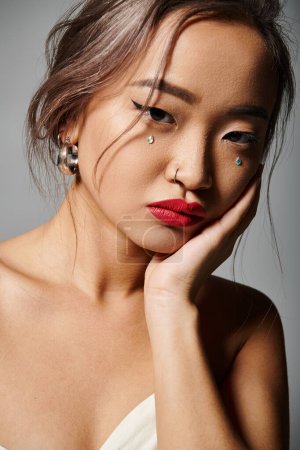 Téléchargez les photos : Portrait de attrayant asiatique jeune femme couvrant la joue avec la main sur fond gris - en image libre de droit