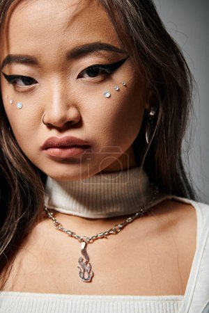 schöne asiatische junge Frau in stilvollem Outfit mit gewagtem Make-up vor grauem Hintergrund