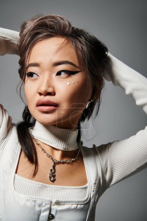 Porträt einer asiatischen Frau mit gewagtem Make-up, die die Hand hinter den Kopf legt und nach unten schaut