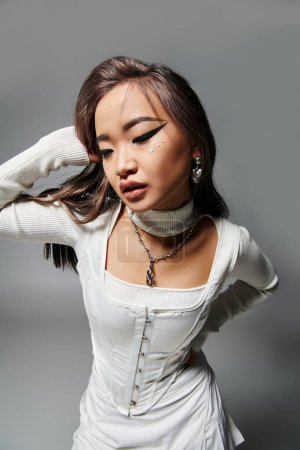 attraktive junge Frau in stylischem Outfit mit gewagtem Make-up posiert mit Händen auf grauem Hintergrund