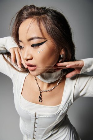 pretty asian girl with daring makeup posing with hands near face and looking to down