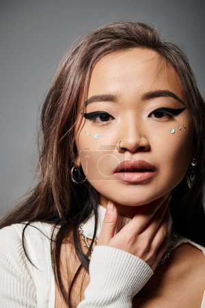 close up of attractive asian woman in her 20s with outrageous makeup against grey background