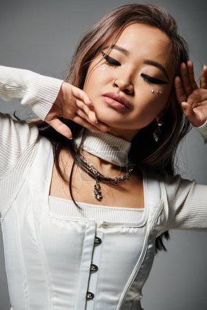 alluring asian woman in her 20s closing eyes with hands around to face on grey background