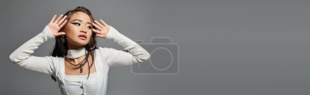 Photo for Horizontal shot of asian woman in 20s looking to side and posing with hands against grey background - Royalty Free Image